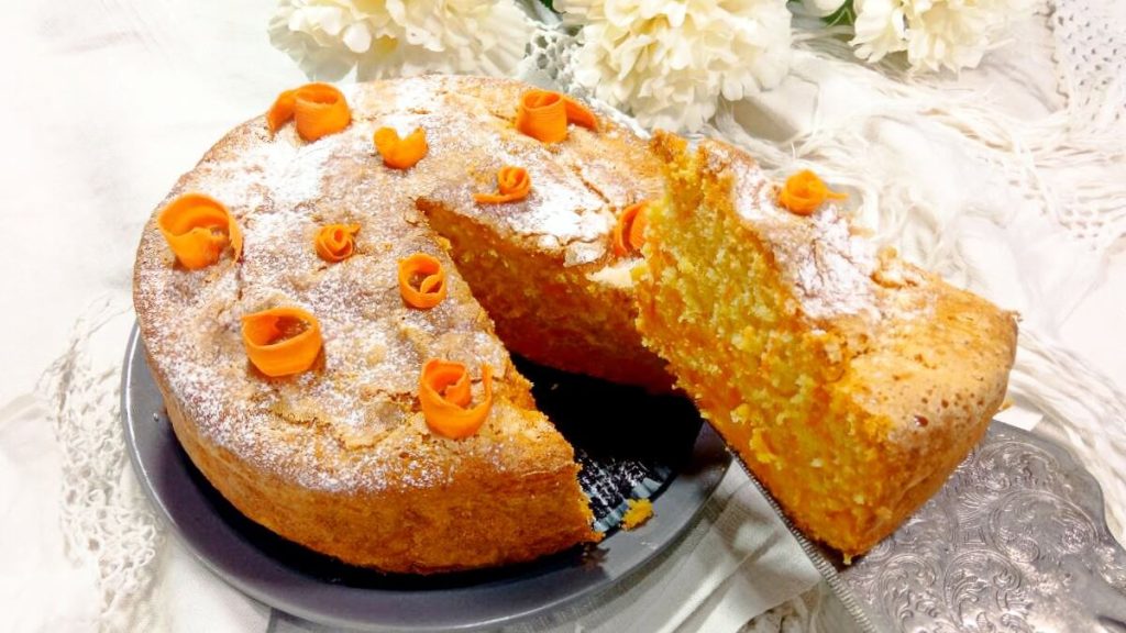 Torta di carote senza burro soffice Ricette SOS – fetta sollevata con decorazioni arancioni e zucchero a velo